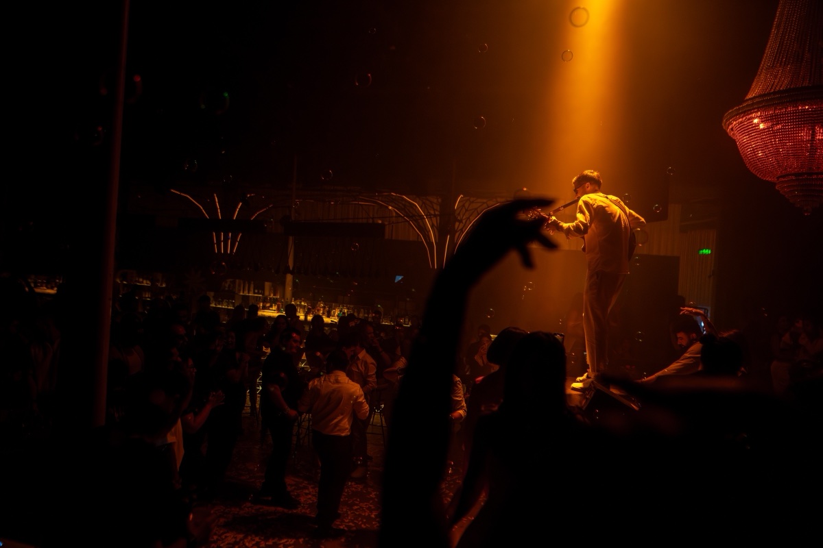 A performer lit from above on a podium in a warm, crowded venue