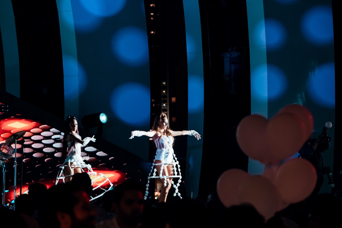 Two dancers on a raised blue-lit stage seen over the crowd