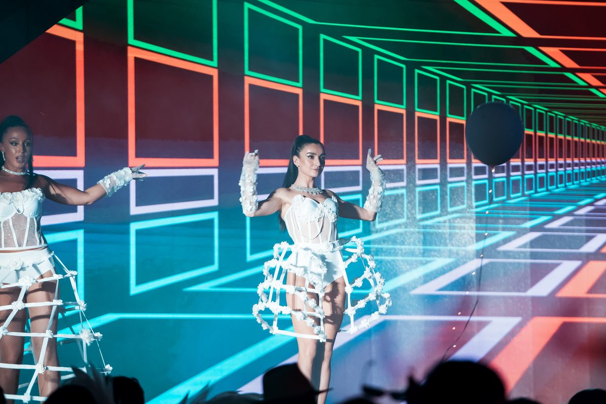 Performers in illuminated wire costumes in front of a neon LED wall