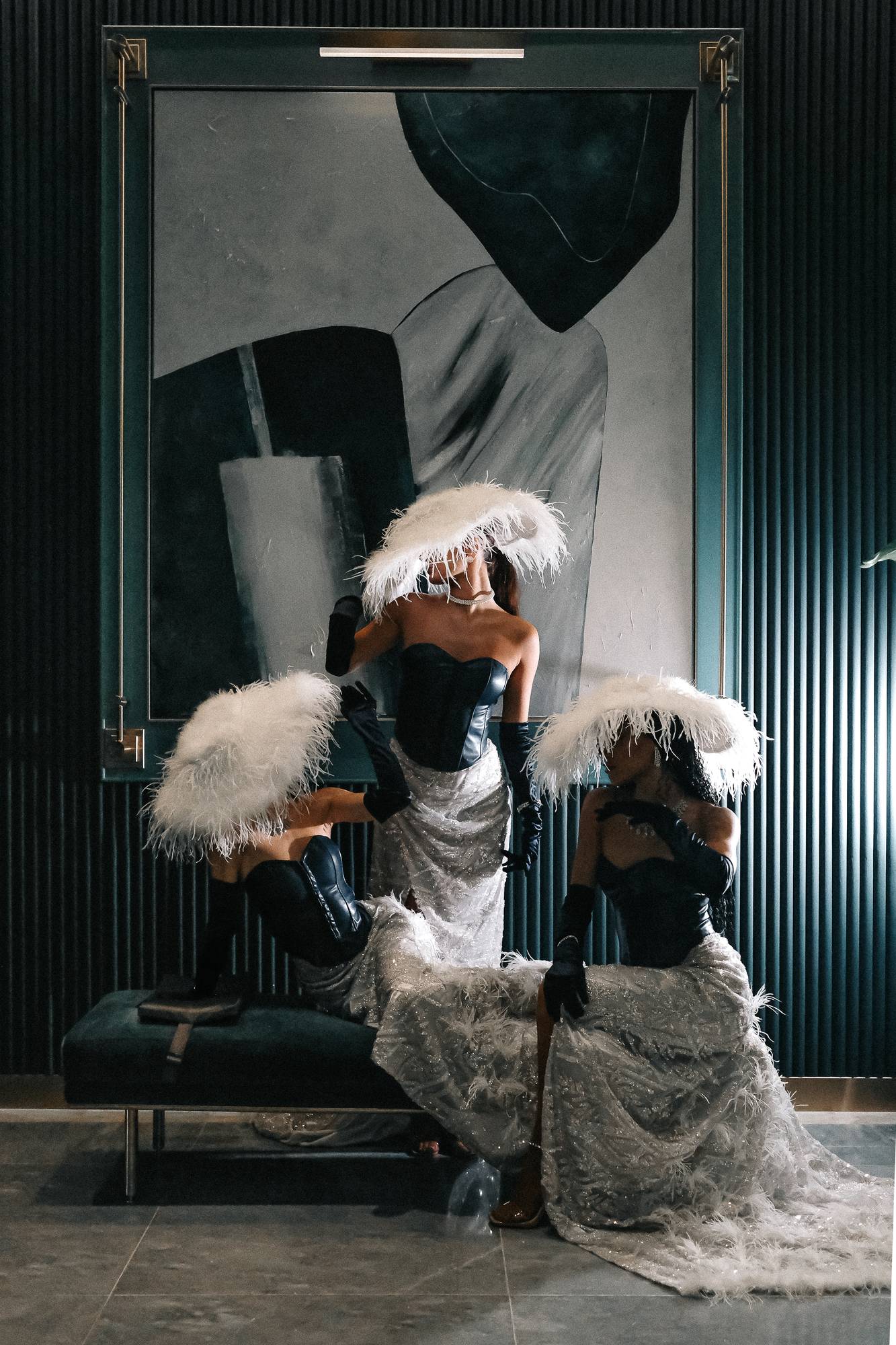 Two performers in white feather hats and corsets in a dark lounge interior