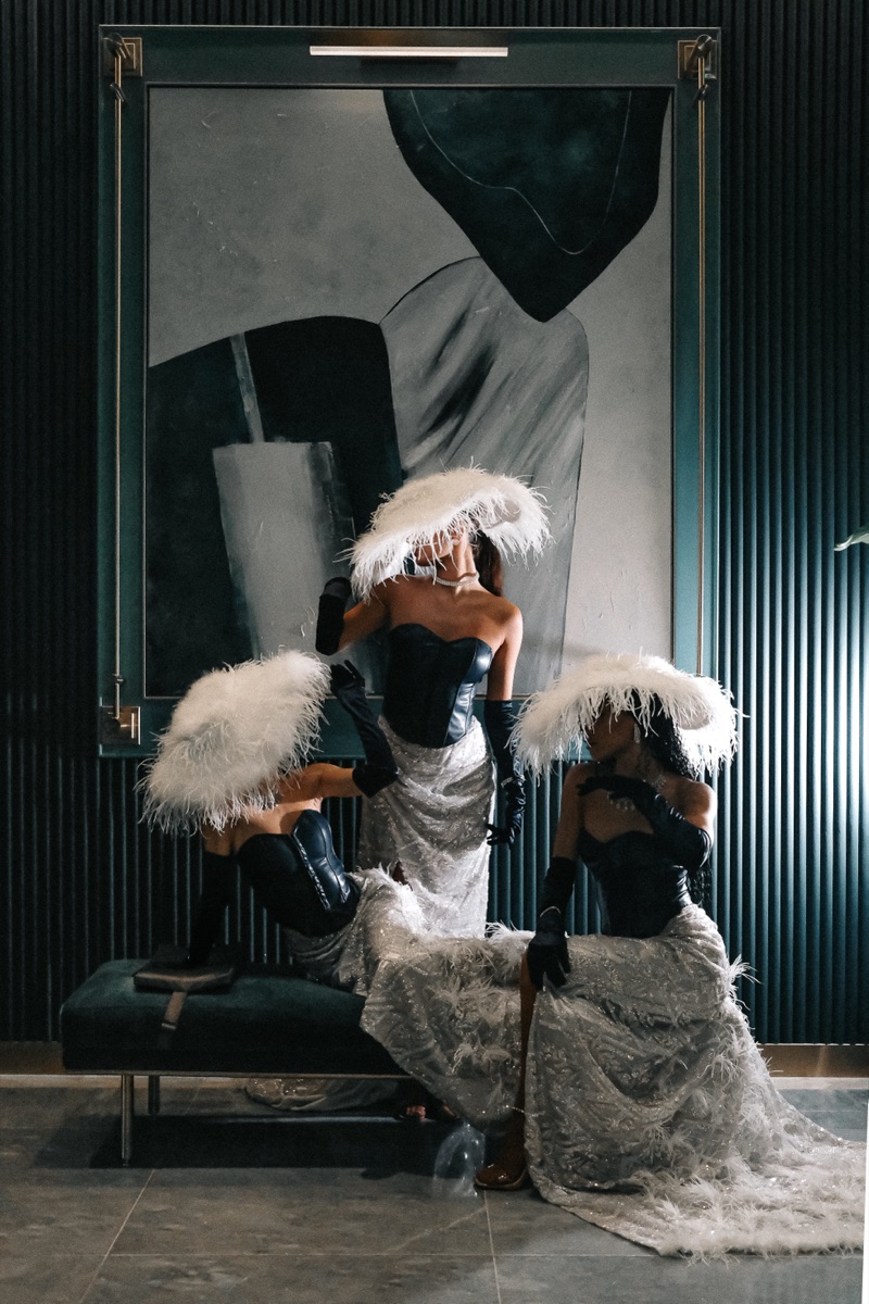 Three performers in feather hats and corseted gowns posed around a bench