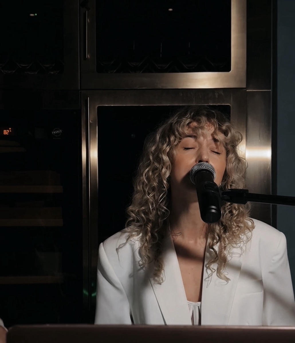 A vocalist singing into a microphone in a white blazer