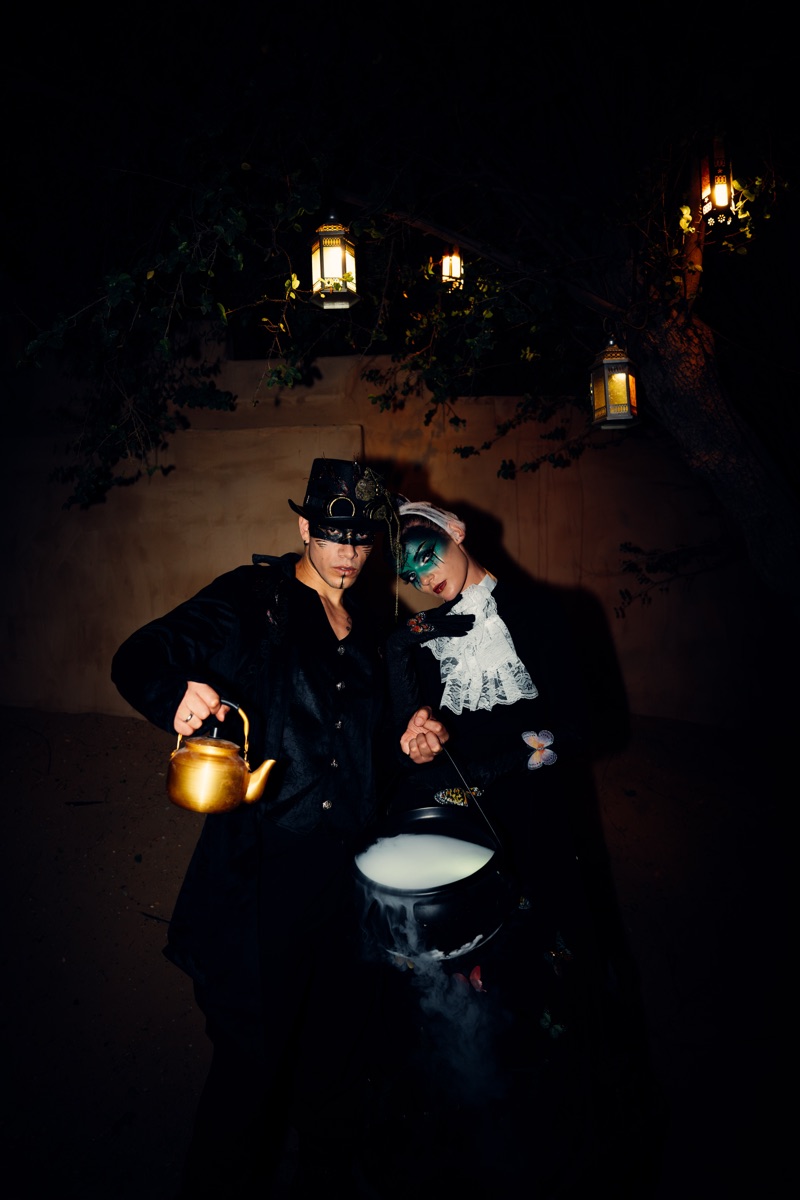 Two masked Halloween performers pouring a golden teapot into a smoking cauldron
