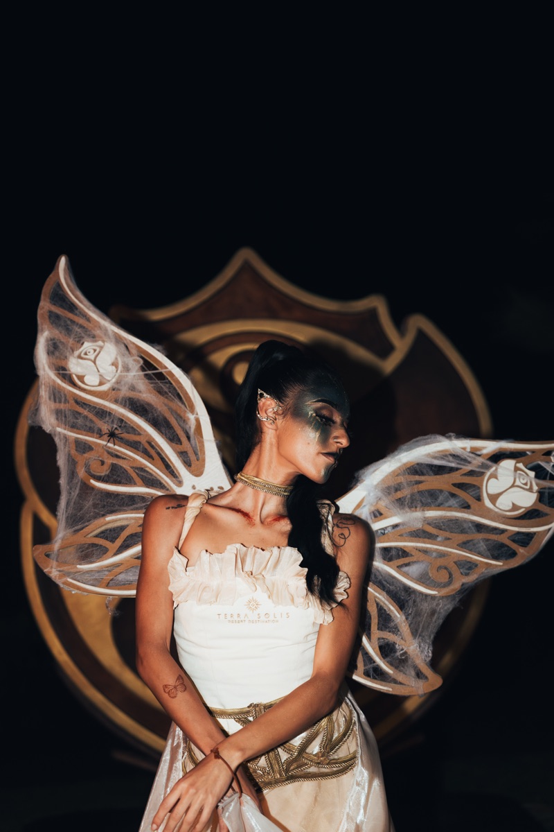 A performer with lace fairy wings and gold face paint in an ivory gown