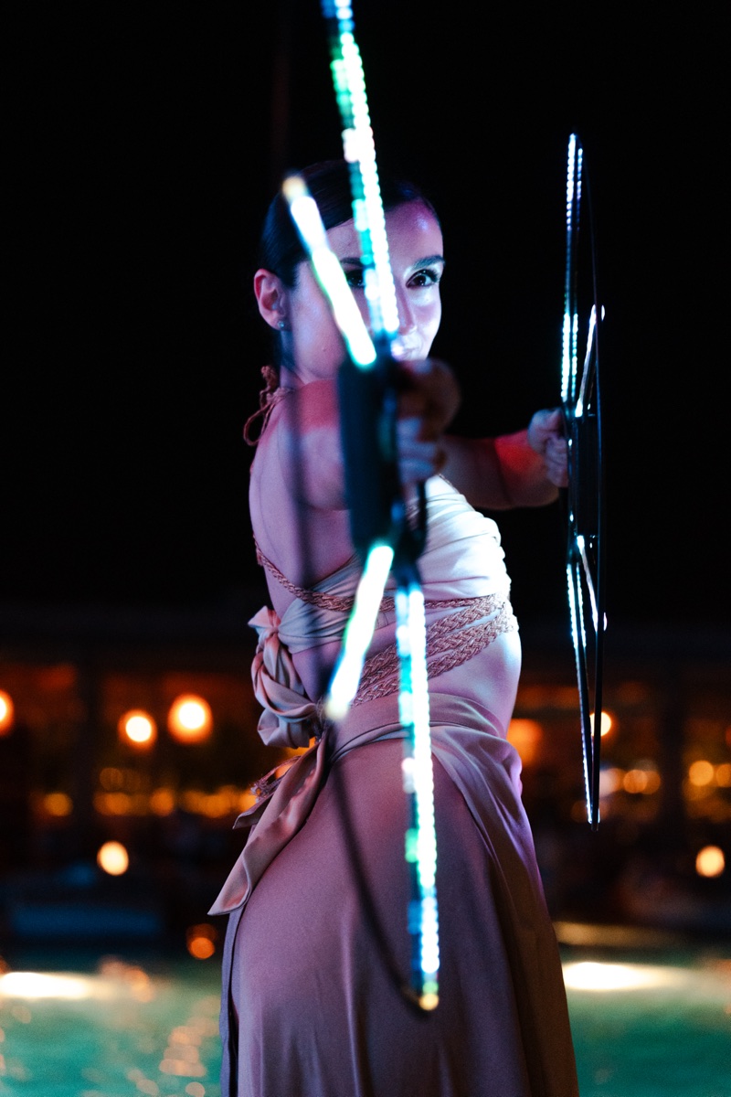 A performer spinning illuminated LED staffs beside the pool at night