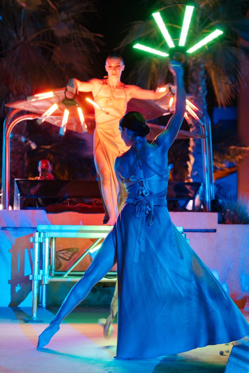 Two performers with LED fan props under palm trees at night