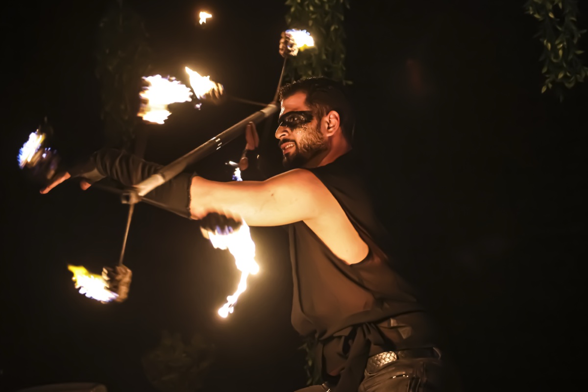 A fire performer spinning a flaming staff, trails of fire arcing around him