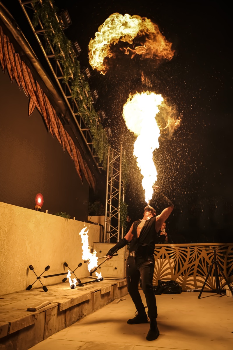 A fire-breather sending a fireball into the night sky above a terrace stage