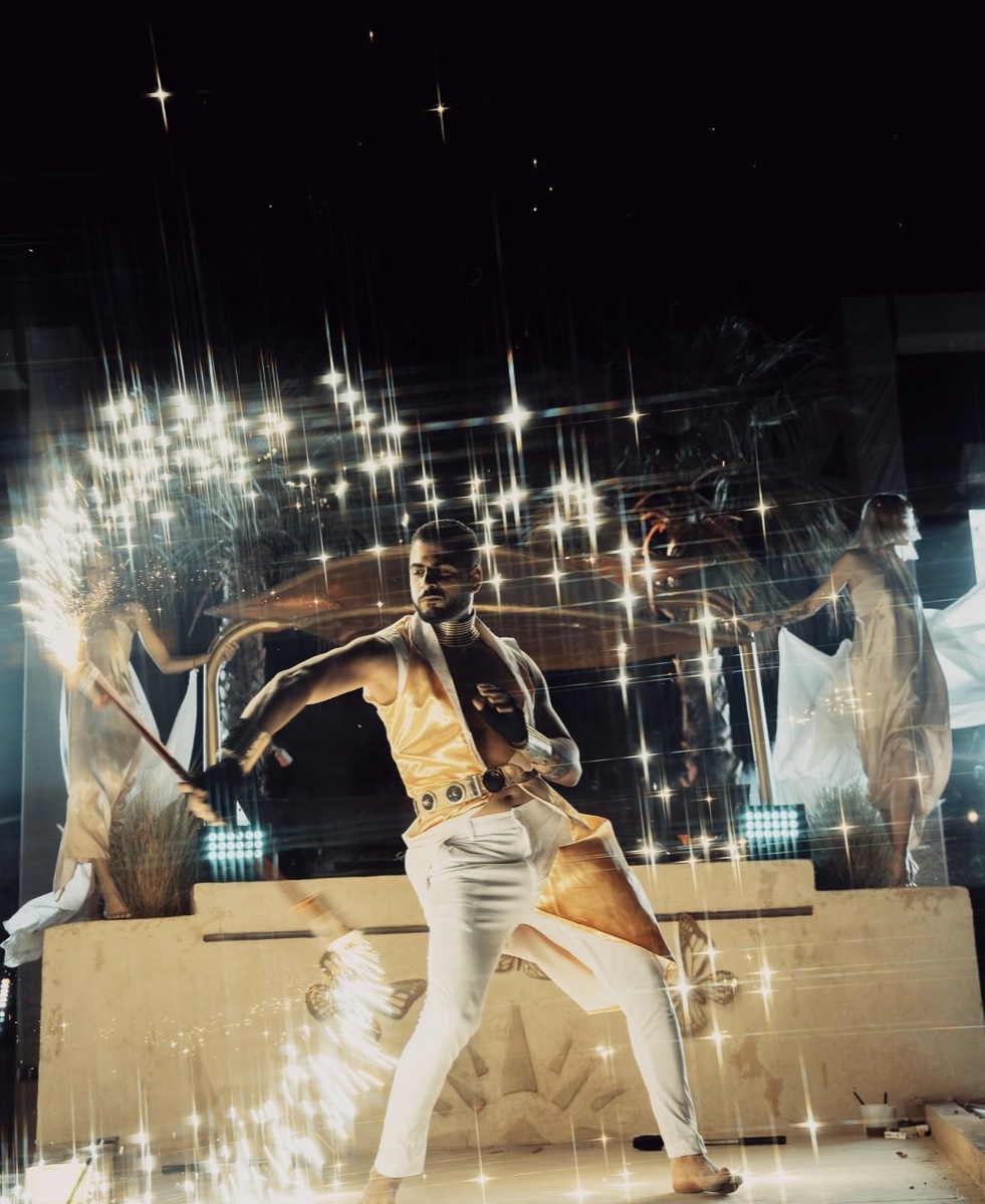 A performer mid-move on a tiered stage as sparks fall around him