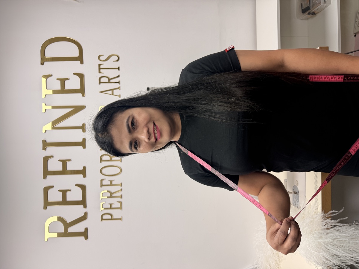 Our tailor holding a measuring tape in the atelier, gold lettering behind her