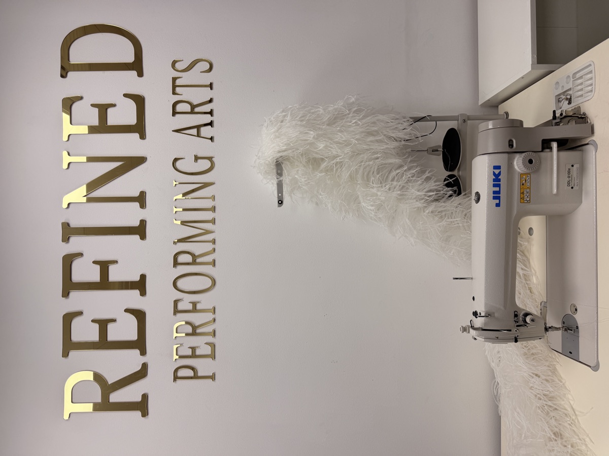 The Refined atelier — gold lettering above an industrial sewing machine and white feathers
