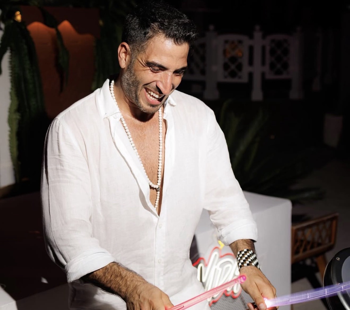 A percussionist in a white linen shirt smiling behind his kit at a beach club