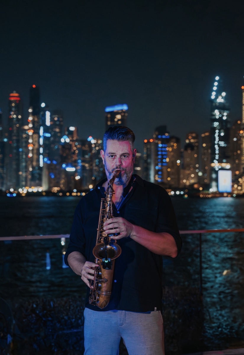 A saxophonist playing against the lit Dubai skyline at night