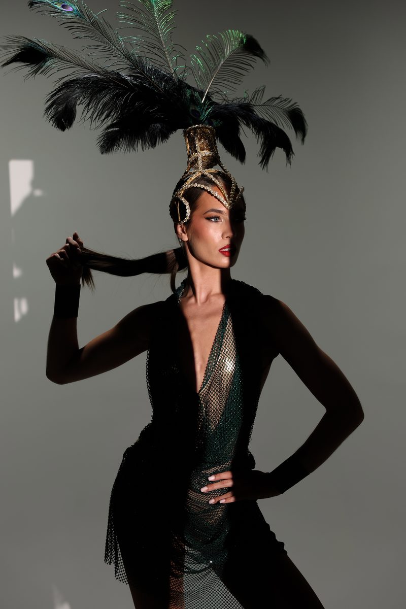 A performer in a dark feathered headdress lit by a single dramatic light