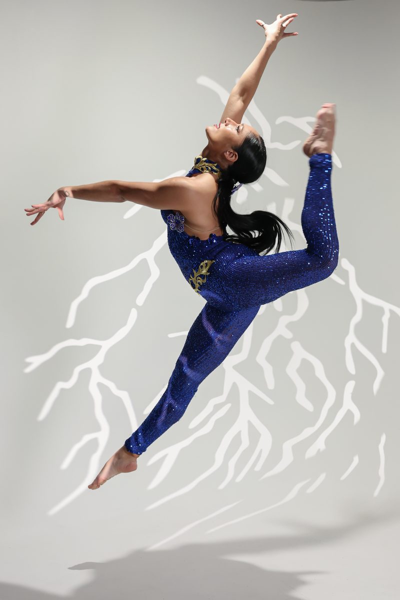 A Refined dancer in a blue sequinned jumpsuit mid-leap