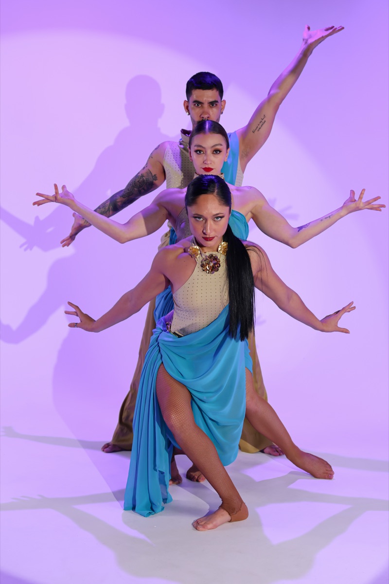 Three dancers in gold and turquoise costumes stacked in a layered studio pose