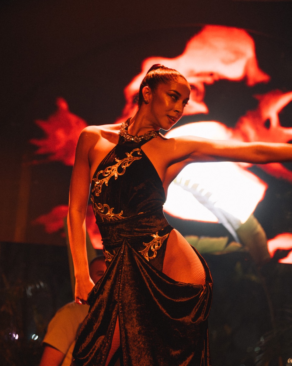 A dancer in a black velvet gown with gold embroidery mid-move on a club floor