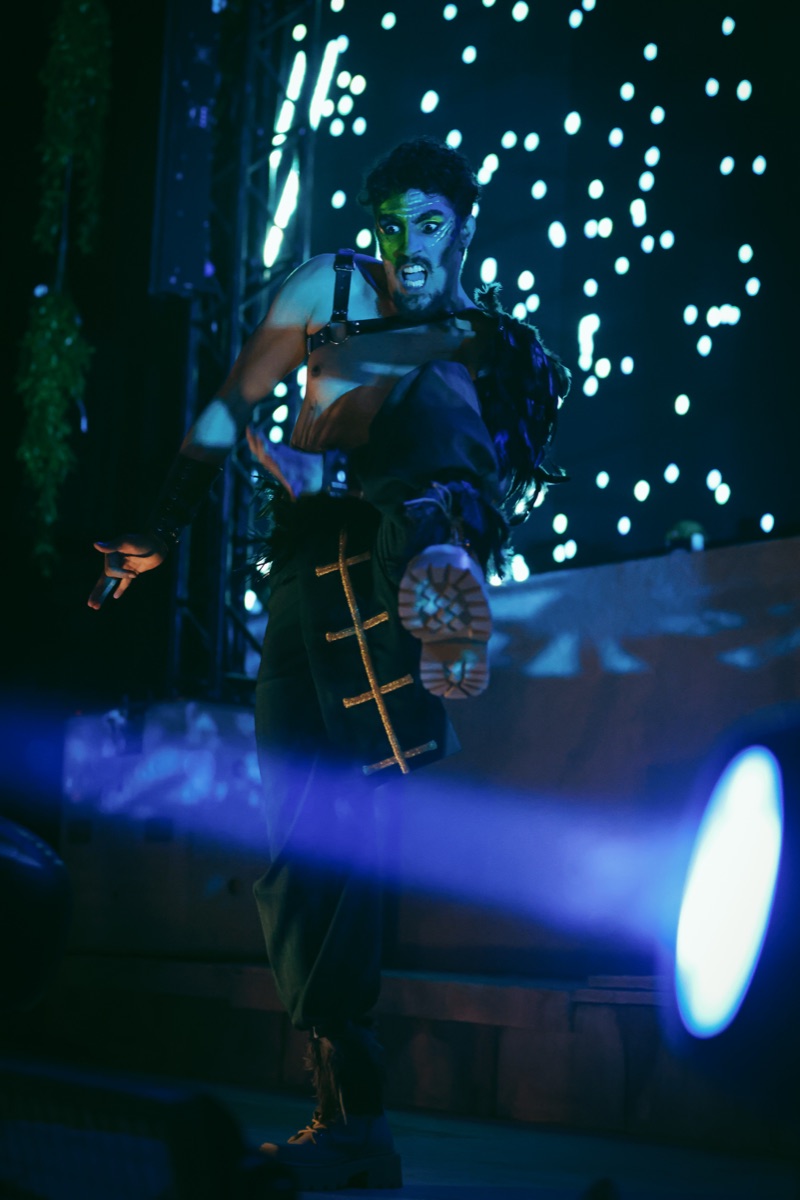 A performer kicking toward camera before an LED starfield wall, a blue beam crossing the frame