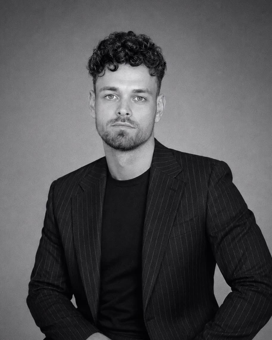 Jordi, growth advisor at Refined Performing Arts, in a black and white portrait wearing a pinstriped jacket