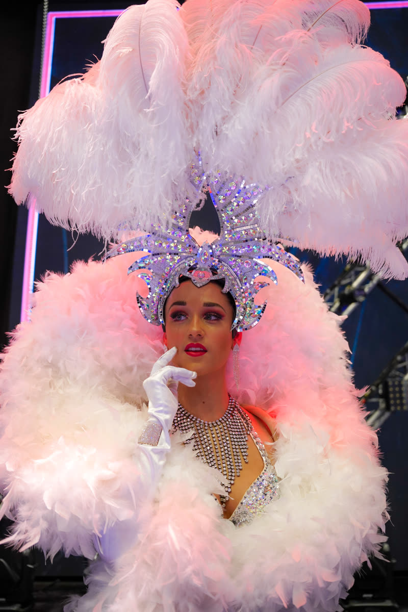 Laura performing as a showgirl in a pink and white ostrich feather headdress and crystal costume