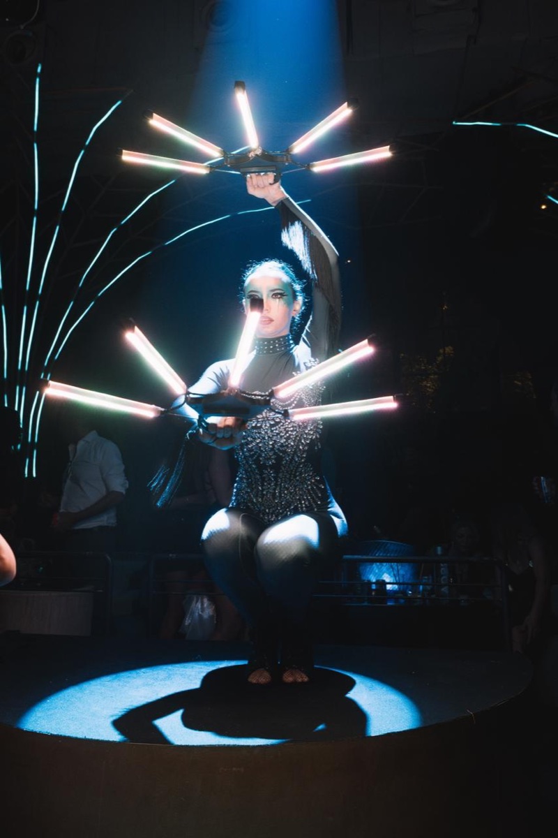 A performer holding glowing LED fan blades overhead in a darkened venue