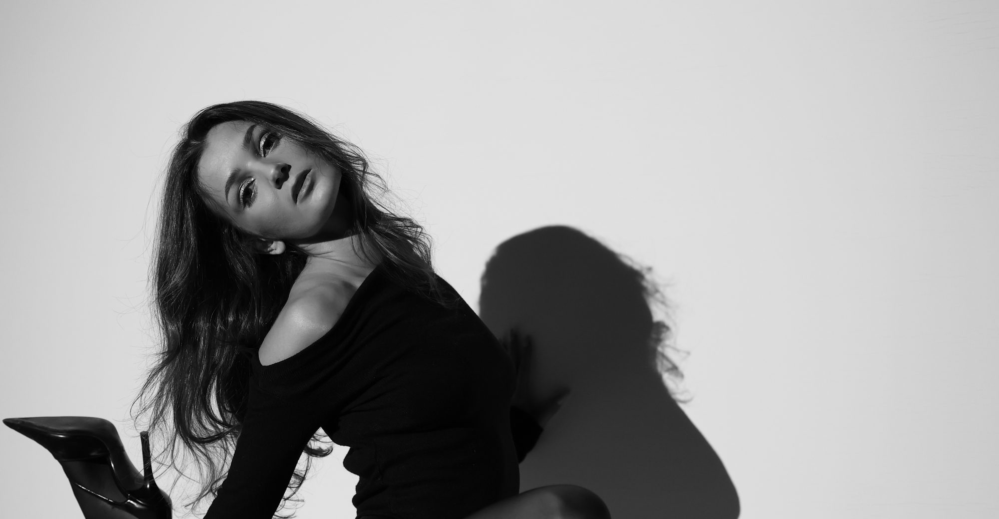 A dancer in a black bodysuit and heels casting a long shadow across a studio wall