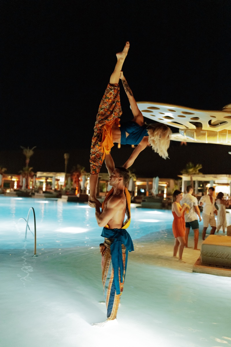 Two performers together on a lit walkway between the pools at Terra Solis at night